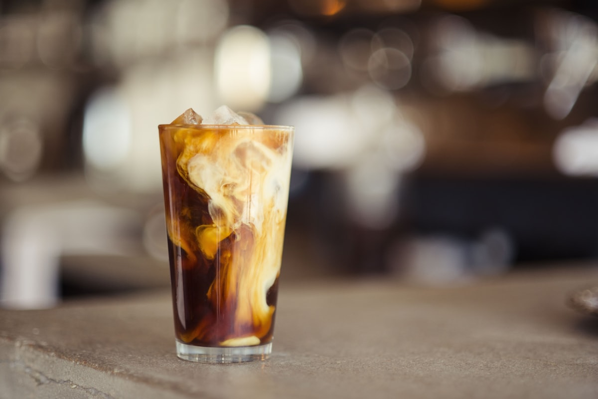 A tall glass of iced cold brew coffee with cream swirling through it