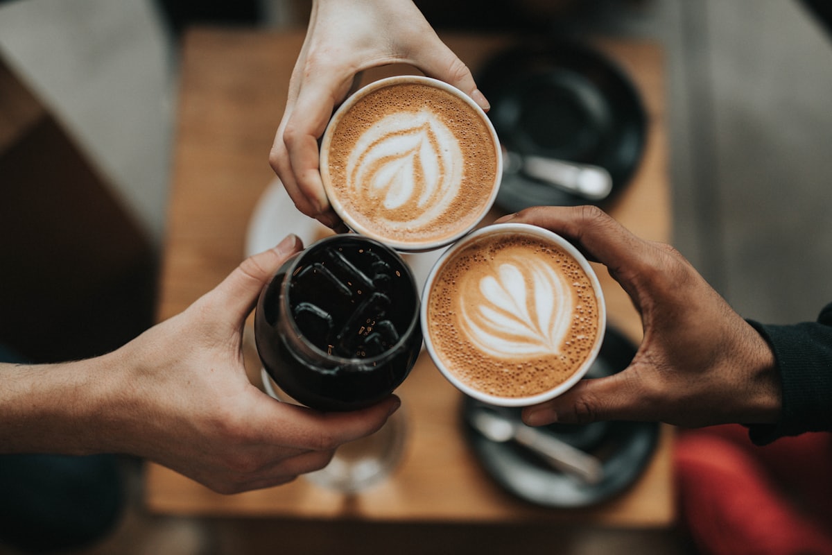 Three hands toasting with lattes and a cold brew, latte art on the foam