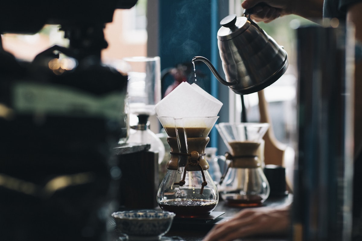Pour-over coffee brewing into a glass carafe as water streams from a gooseneck kettle