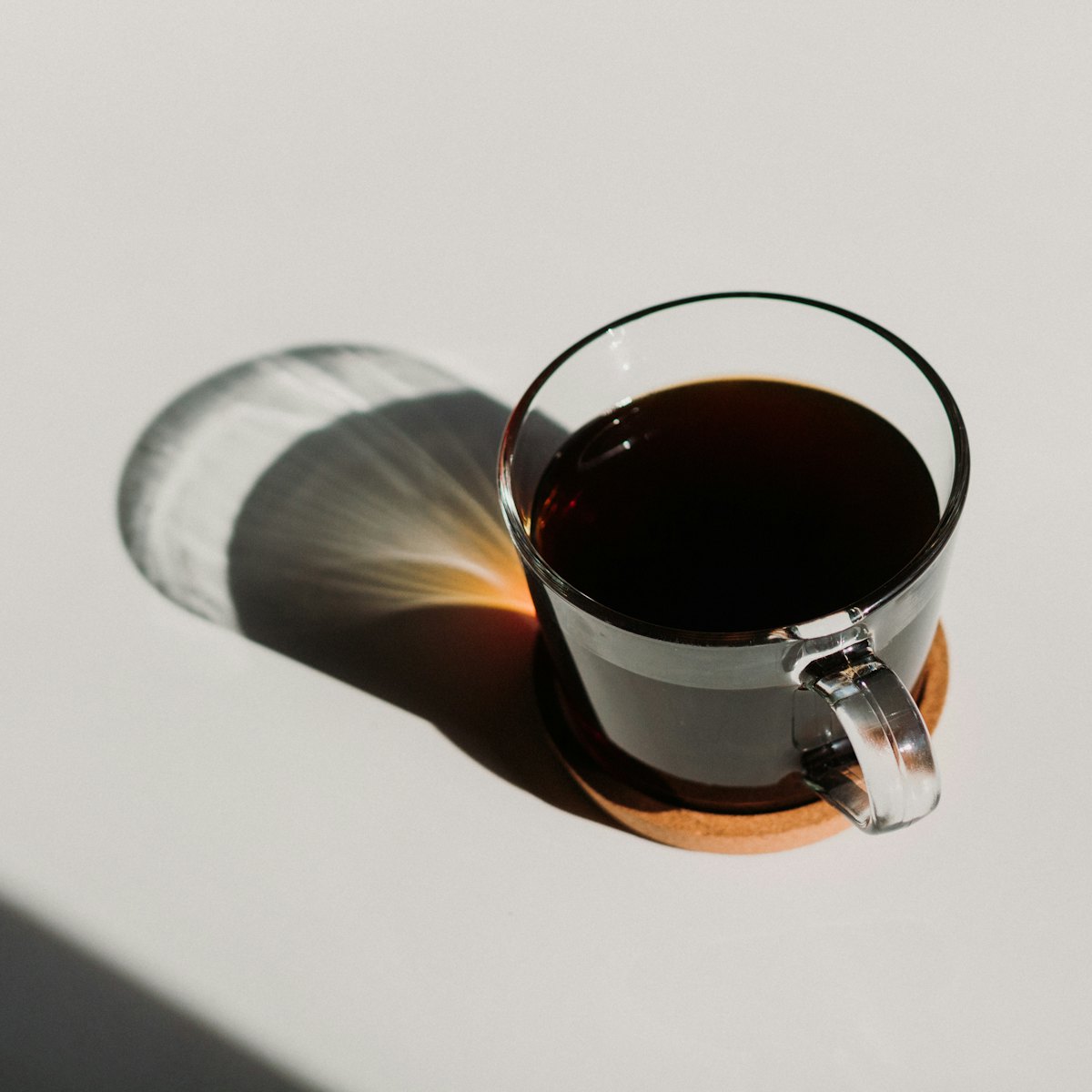 A glass cup of black coffee in soft morning light casting a long shadow