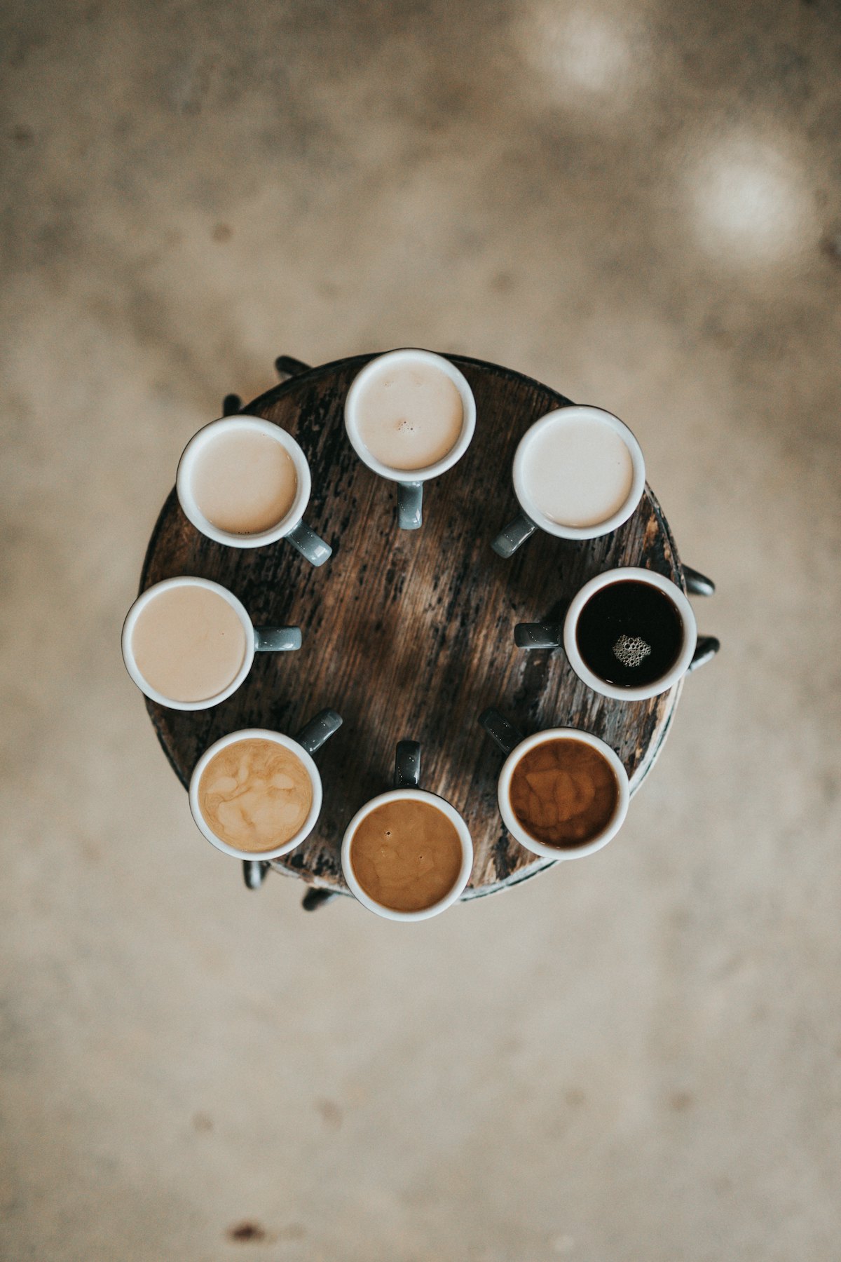 Eight cups of coffee arranged in a circle on a wooden stool, seen from above