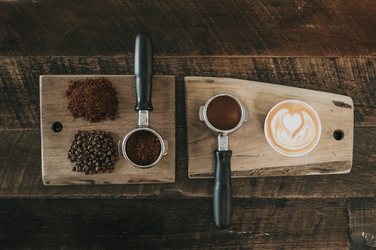 An espresso portafilter of fresh grounds beside whole beans and a latte